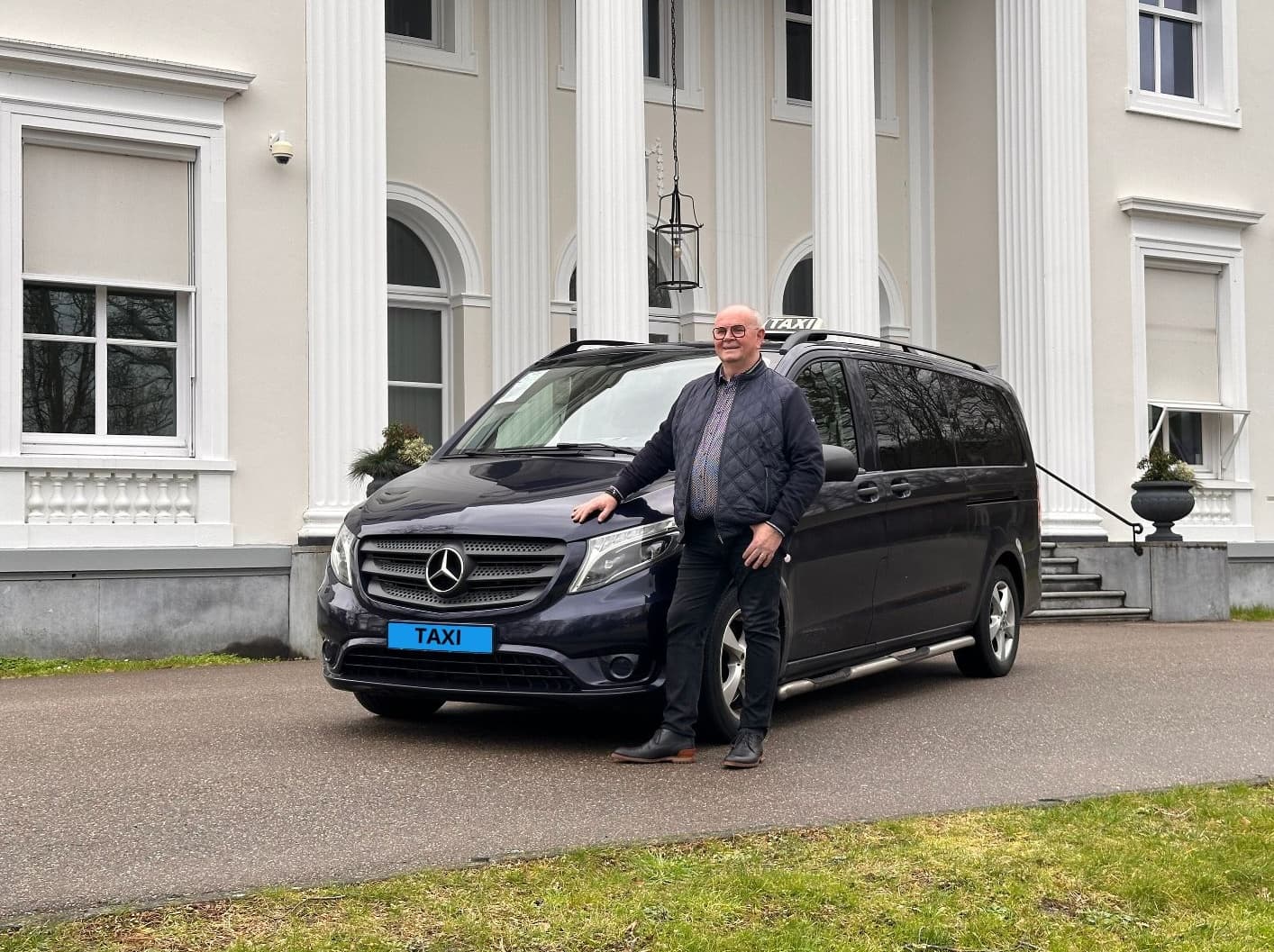 Ronald Hirs samen met zijn donker blauwe Mercedes taxibus.